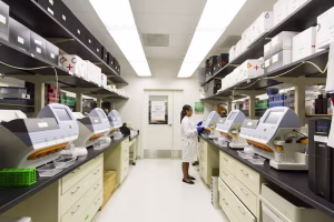 Laboratory technician standing between rows of analytical instruments.